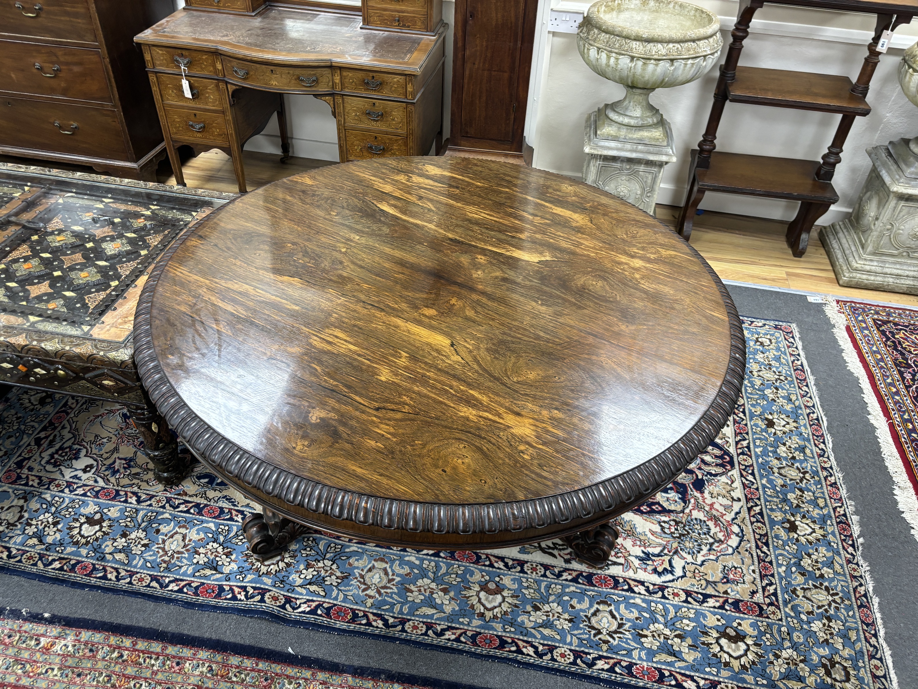 A William IV circular rosewood centre table, the tilt top with lappet carved edge on single tapered hexagonal column, tripartite slab base with scrolled feet, diameter 135cm, height 72cm